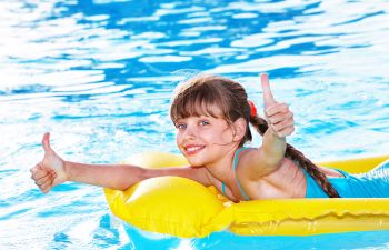 A happy girl floating on an inflatable ring in swimming pool showing her thumbs up.